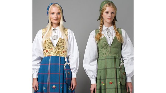 To kvinner iført tradisjonelle bunader med broderte detaljer og skjorter, stående side om side.