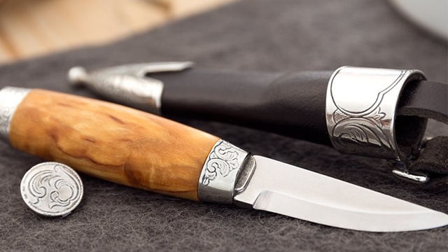 En tradisjonell kniv med treskaft og dekorativt blad, plassert ved siden av en lærslire og en metallmynt.