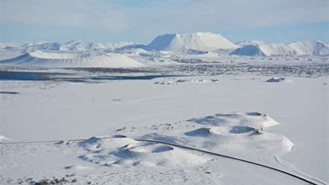 Vinterlandskap med snødekte fjell, innsjø og snødekte åser i bakgrunnen.