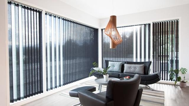 Moderne stue med svarte persienner, en svart sofa, et rundt bord og en dekorativ lampe i taket.