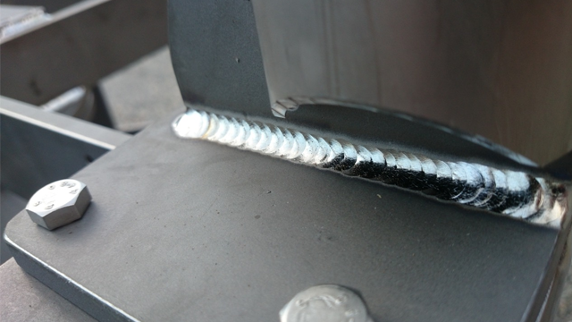 Sveisefuge på metallramme med tydelige sveisestriper og bolter synlige i nærheten.