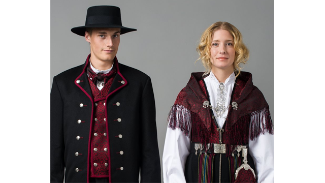 Mann og kvinne iført tradisjonelle norske bunader med hatter og detaljerte broderier.