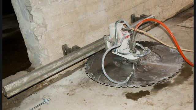 En stor betongsag med en rund sagblad, plassert på et betonggulv i en kjeller.