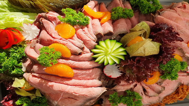 Et fargerikt fat med roastbiff, grønnsaker, sitrusfrukter og friske urter som pynt.