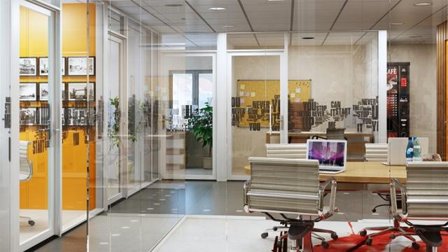 Moderne kontorinnredning med glassvegger, skrivebord og stoler, samt planter og kreative elementer på veggene.