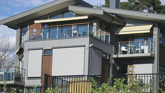Moderne hus med store vinduer, balkonger og terrasse, omgitt av grøntområder.