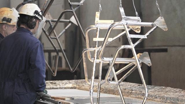 To personer i arbeid med metallrammer som henger fra taket i en fabrikk.