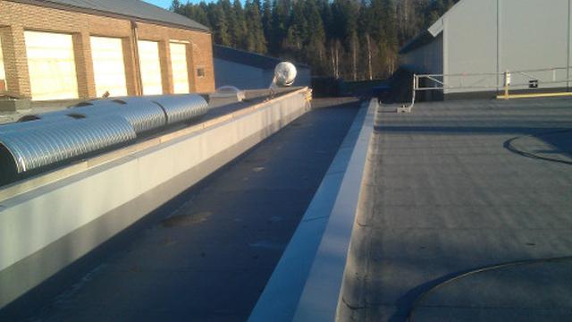 Tak med avrenningskanal og ventilasjonsrør på en bygning i skogen.