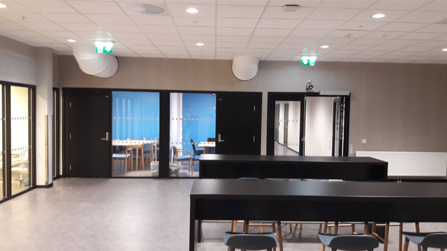 Moderne møterom med svarte bord og stoler, glassdører som fører til et lyst rom med blå vegger.