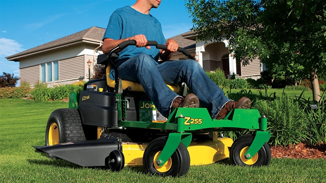 Mann som klipper gresset med en gressklipper av typen John Deere Z255 i en hage foran et hus.