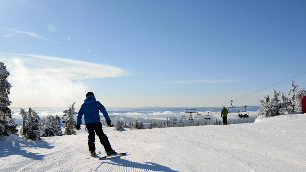 En snowboarder på en snødekt bakke med fjellutsikt og stolheiser i bakgrunnen.