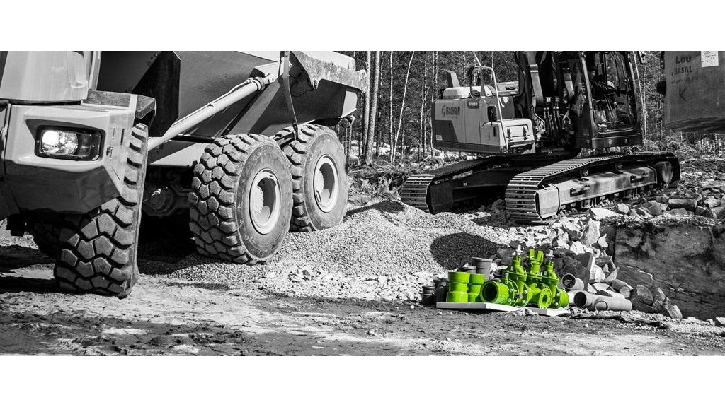 Grønn rørleggerutstyr ligger på bakken ved siden av en gravemaskin og en dumper i et byggeområde.