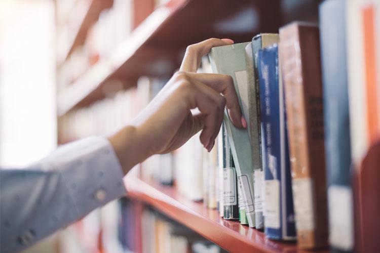En hånd tar en bok fra en bokhylle fylt med bøker i et bibliotek.