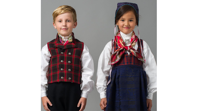 To barn i tradisjonelle norske bunader, en gutt med vest og en jente med kjole og skjerf.