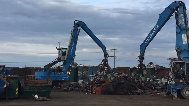 To store med skrapmetall og to kraner som løfter metallbiter på en gjenvinningsplass.