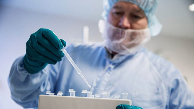 En laboratorietekniker i beskyttelsesutstyr bruker en pipette til å overføre væske til prøverør.