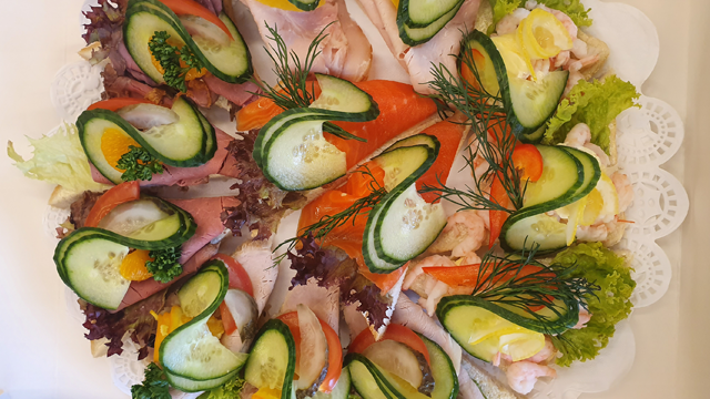Et fat med variert pålegg, inkludert skiver av røkt laks, skinke, reker, agurk og salat.