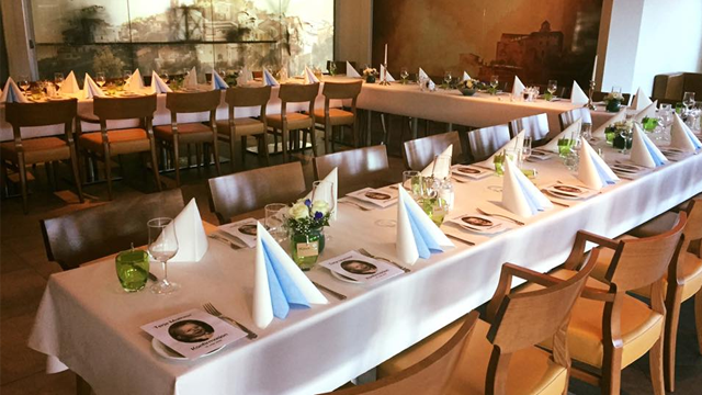 Et elegant restaurantbord dekket med hvite duker, blå servietter og blomsterdekorasjoner.