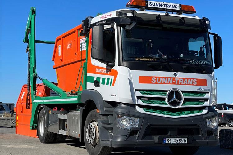 En søppelbil fra Sunn-Trans med oransje og grønn container, parkert på en solfylt dag.