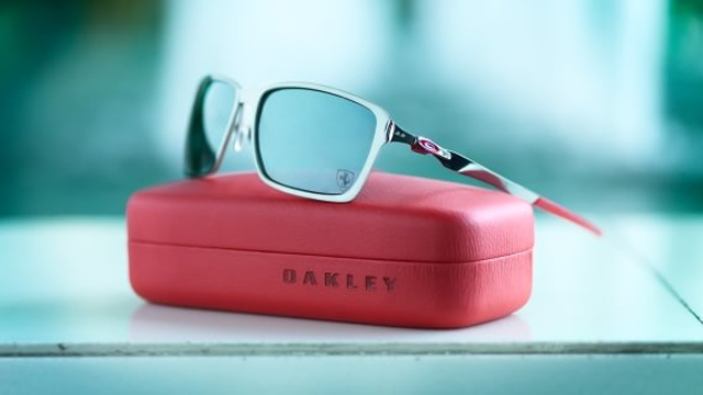Sorte solbriller fra Oakley liggende på en rød etui med refleksjoner i bakgrunnen.