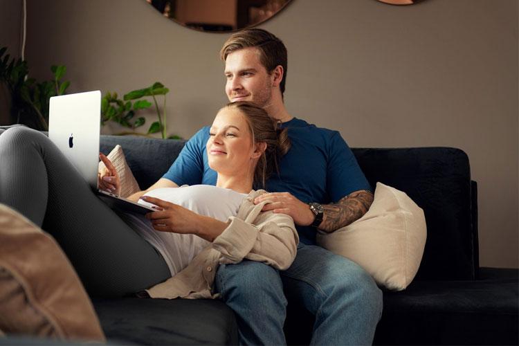 Et par sitter sammen på en sofa og ser på en laptop, med en avslappet og koselig atmosfære.
