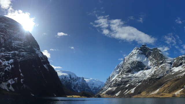 Fjorder med snødekte fjell og klar blå himmel, sollys som skinner over landskapet.