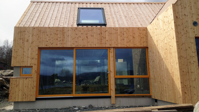Moderne hus med trepanel og store vinduer, beliggende i naturskjønne omgivelser.