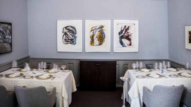Et elegant restaurantinteriør med to dekkede bord og moderne kunstverk på veggen.