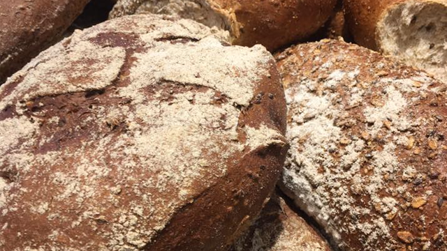 Nærbilde av ferske brød med grovt mel og sprø skorpe, stablet på en bakeribenk.