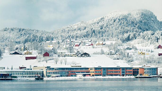 Vinterlandskap med snødekte fjell og fargerike hus ved vannkanten.