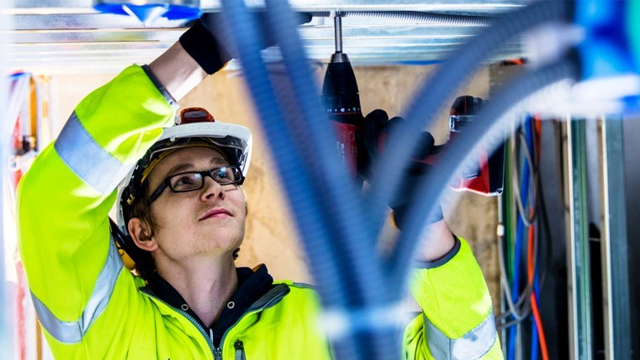 En elektriker i sikkerhetsutstyr jobber med en drill under installasjon av elektriske systemer.