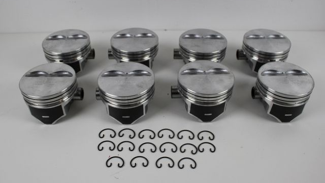 Åtte motorstempler i metall med tilhørende O-ringer på en hvit bakgrunn.