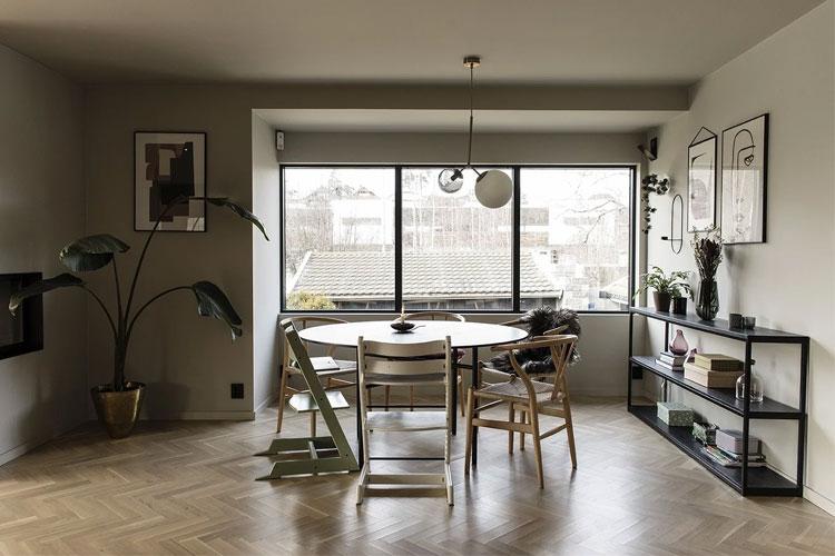 Moderne stue med stort vindu, rundt bord, stoler og stilige planter i en lys og minimalistisk innredning.