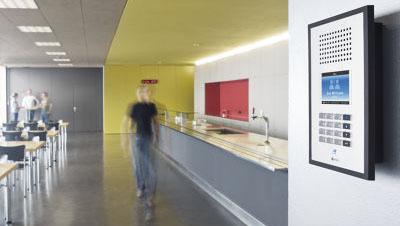 Moderne kantine med en person som går forbi, en digital skjerm og en lys gul vegg.