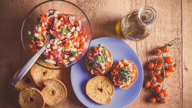 Frisk salat med tomater og løk i en bolle, servert med brødskiver og olivenolje på et trebord.