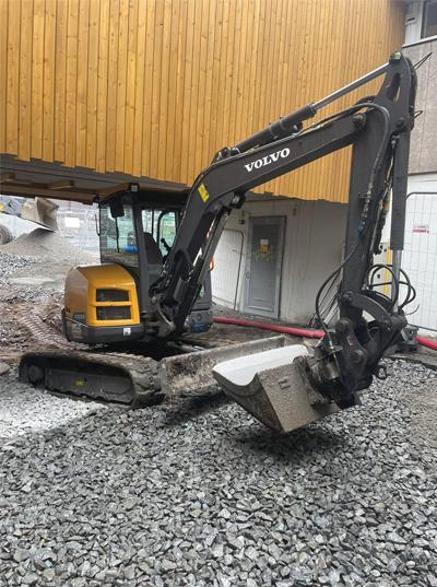Gravemaskin fra Volvo som arbeider med grus under en bygning.