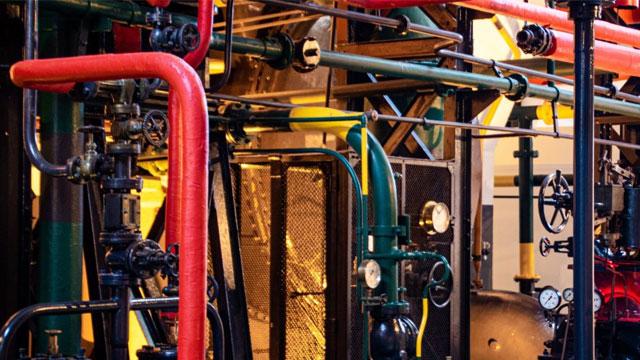 Rørledninger og ventiler i en industriell maskin, med fargerike rør og måleinstrumenter synlige.