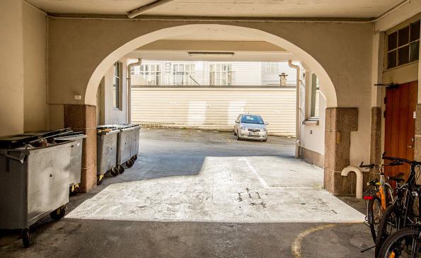 Utsikt gjennom en bue i en garasje med søppeldunker og en bil parkert i bakgrunnen.