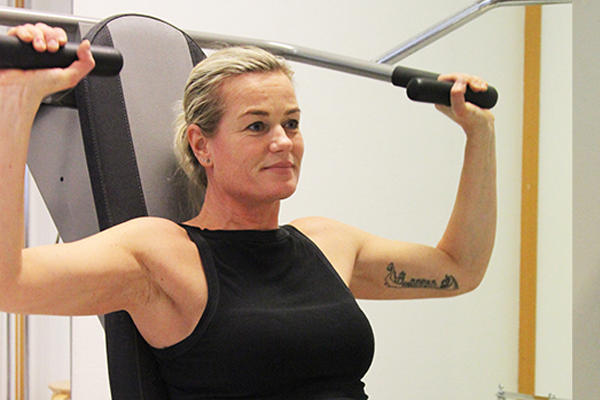 Kvinne som trener styrketrening med vektstang på treningsstudio.
