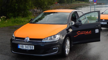 En svart Volkswagen med oransje tak og åpen dør, parkert ved en elv.