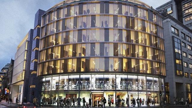 Moderne bygning med glassfasade og mange mennesker utenfor, beliggende i en bygate.