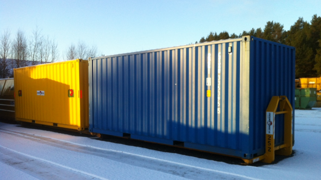 To store containere i forskjellige farger, en gul og en blå, plassert på snødekt grunn.