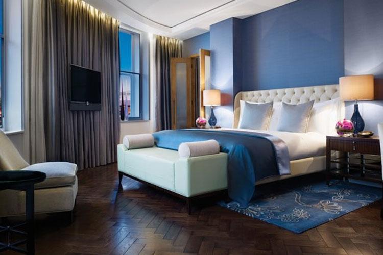 Luksuriøst hotellrom med blå vegger, stor seng, moderne møbler og myke gardiner.