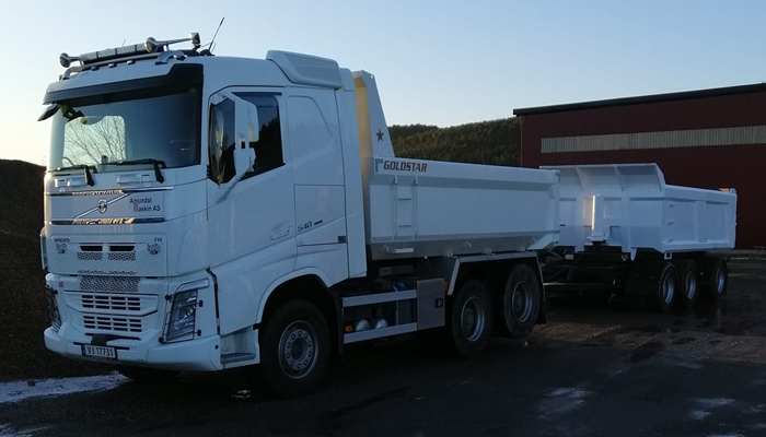 En hvit lastebil med tilhenger står parkert på en byggeplass, klar for transport av materialer.