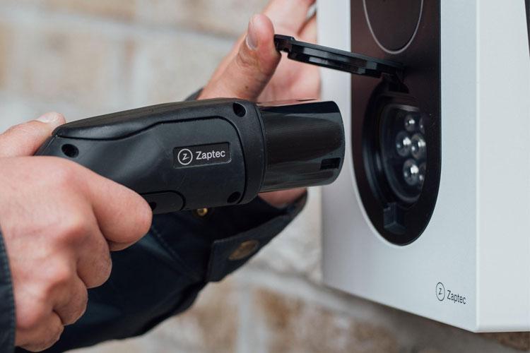 En person bruker en ladekabel for å lade en elektrisk bil ved en ladestasjon.