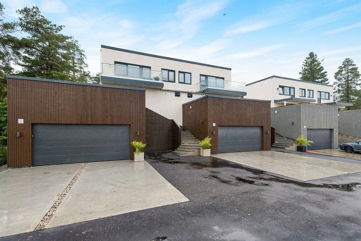 Moderne boliger med garasjer og trapper, omgitt av trær og blå himmel.
