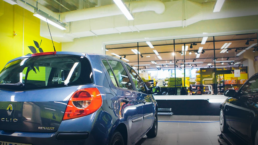 Blå Renault bil i en moderne bilutstillingslokale med gule vegger og store vinduer.