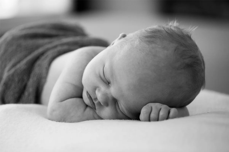 En sovende baby med lys hud og kort hår, liggende på en myk overflate med et teppe.