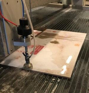 Vannskjærer i aksjon, skjærer gjennom en flis med vannstråle på en arbeidsbenk.