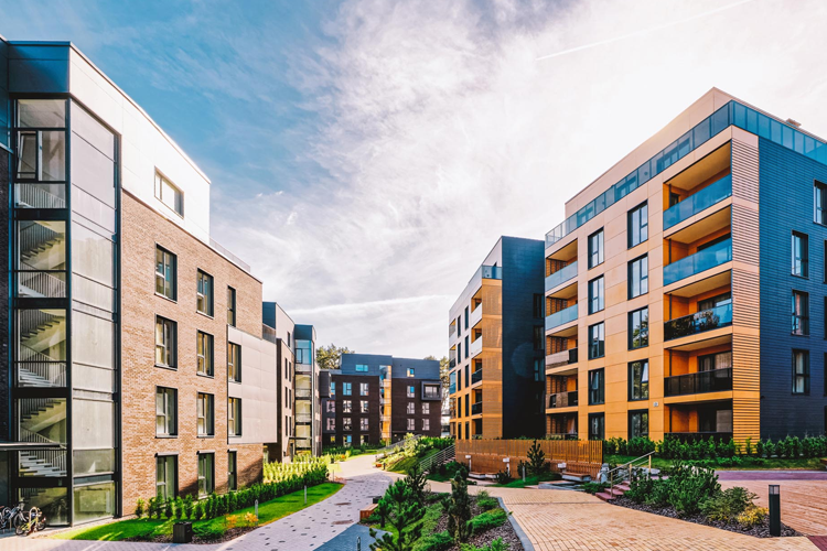 Moderne leilighetskompleks med tre bygninger, grønne områder og en solfylt himmel.